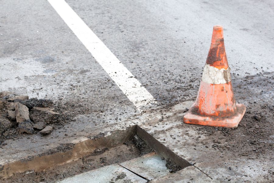 A damaged cone beside a hole in the road